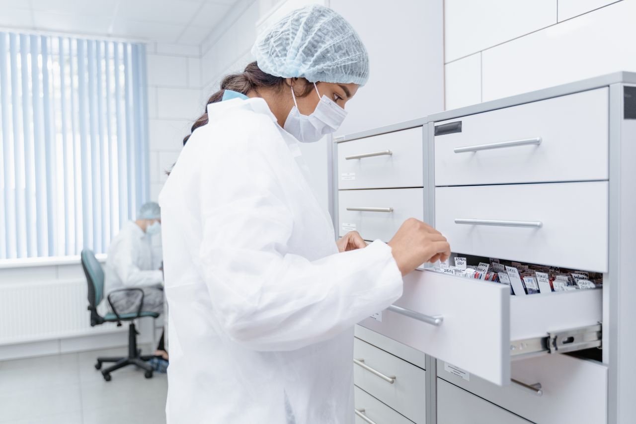 Female scientist in lab coat checks samples in laboratory drawers.